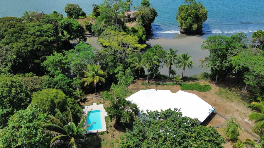 Vista aérea de la piscina del Club House Pacífico Hostel rodeada de palmeras junto al mar
