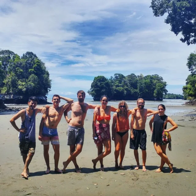 Siete viajeros juntos en la arena de Playa Escondida, con islotes y selva al fondo